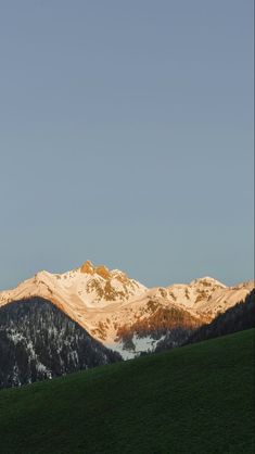 the mountains are covered in snow and green grass as the sun is setting on them