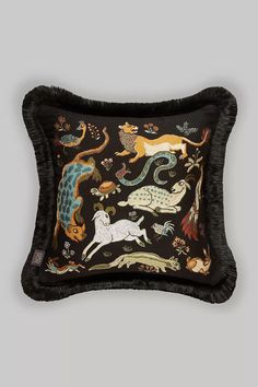 an embroidered pillow with various animals on black and brown fur trimming, sitting on a gray background