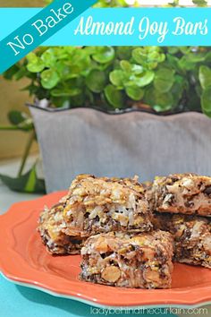 no bake almond joy bars are stacked on an orange plate next to a potted plant