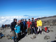 a group of people standing on top of a mountain with mountains in the background and clouds