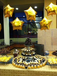 a table topped with lots of desserts covered in gold foil star balloons and chocolate cupcakes