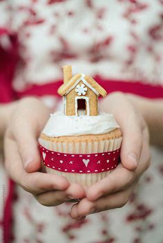 a person holding a cupcake with a house on top