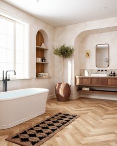 a bath room with a tub a sink and a rug on the floor in front of a window