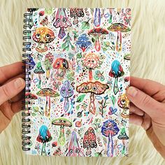 two hands holding a notebook with colorful mushrooms on it