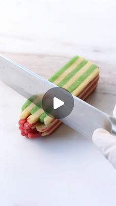 a person holding a large knife over a sandwich cut in half with colored strips on it