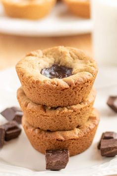 three cookies stacked on top of each other with chocolate chunks next to them and milk in the background