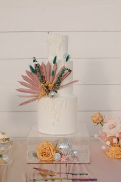 a three tiered white wedding cake with flowers and feathers on the top is surrounded by confetti