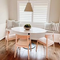 a white table with two chairs and a bowl of fruit on it in front of a window