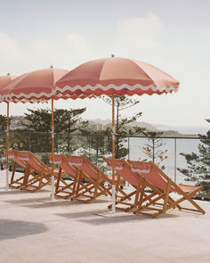 Rows of pink beach umbrellas and deck chairs facing a scenic ocean view. This elegant setup is ideal for a luxurious seaside experience, blending comfort with coastal charm. From Business & Pleasure Co. x Coco Republic collaboration.