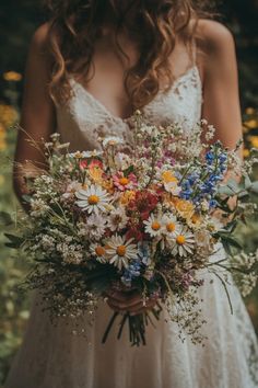 a woman holding a bouquet of flowers in her hands and wearing a wedding dress with lace