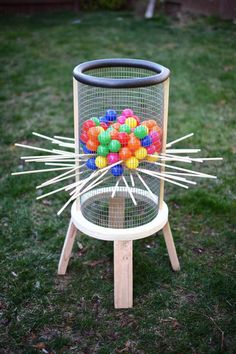 a basket filled with lots of colorful balls on top of a wooden stand in the grass