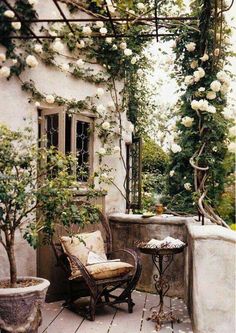 a chair and table sitting on a patio next to a wall covered in white flowers