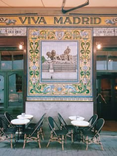 tables and chairs in front of a building with a mural on the wall behind them