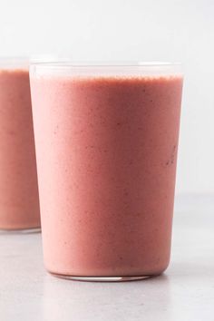 two cups filled with pink smoothie sitting on top of a white counter next to each other