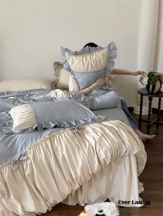 a woman laying on top of a bed covered in blue and white sheets with ruffles