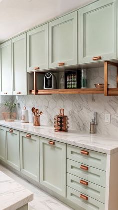 a kitchen with green cabinets and marble counter tops, copper pulls on the cupboards