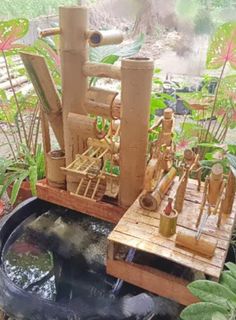 an outdoor fountain made out of bamboo sticks and other items in a garden with plants around it