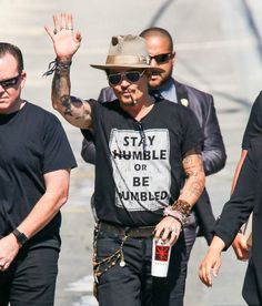 the man is walking down the street with his hand in the air while wearing a hat and sunglasses