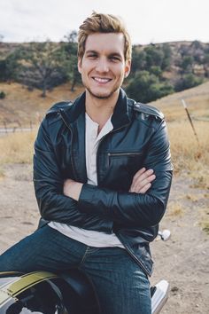 a man sitting on top of a motorcycle smiling at the camera with his arms crossed