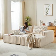 a woman sitting on top of a couch reading a book in a living room next to a window