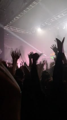 many people are raising their hands up in the air at a concert with bright lights