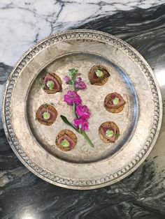 a silver plate topped with small pastries on top of a marble counter next to a purple flower