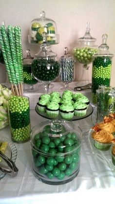 a table topped with lots of green and white desserts covered in candies, candy bars and cupcakes