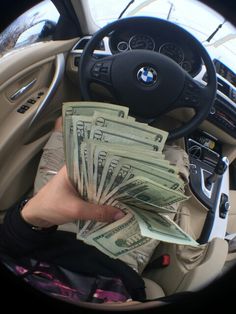 a person holding money in their hand while sitting in the driver's seat of a car