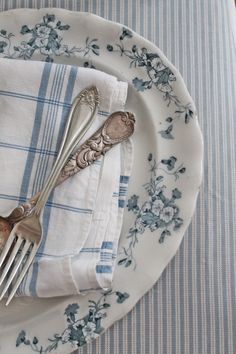 two silver forks on top of a blue and white table cloth with floral design napkins