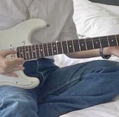 a person sitting on a bed playing an electric guitar with their fingers and thumbnails