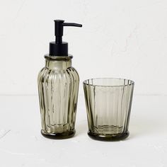 a soap dispenser, glass cup and toothbrush holder on a white surface