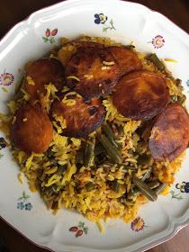 a white plate topped with yellow rice and fried meat covered in green beans on top of a wooden table