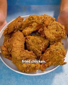 fried chicken on a white plate being held by two hands with the words fried chicken