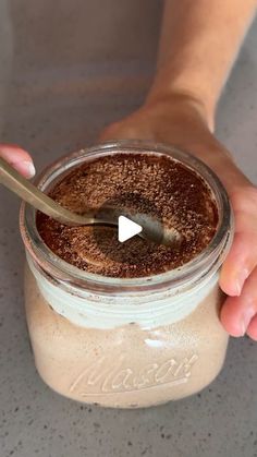 a person holding a spoon in a jar filled with chocolate