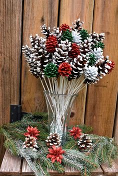 a glass vase filled with pine cones and poinsettis on top of a wooden table