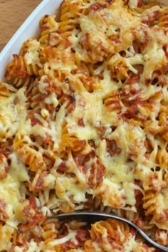 a casserole dish filled with pasta and cheese on a wooden table next to a fork