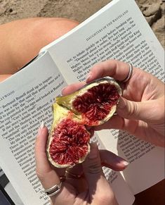 a woman is reading a book and holding a piece of fruit