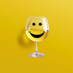 a glass of white wine with a smiley face drawn on it's side, against a yellow background