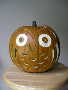 a carved pumpkin sitting on top of a wooden table next to a white wall with an owl face painted on it