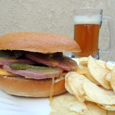 a sandwich and chips on a plate next to a glass of beer