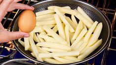 a person is holding an egg in a frying pan over some fries on the stove