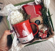 a red coffee mug sitting on top of a green box filled with christmas decorations and marshmallows