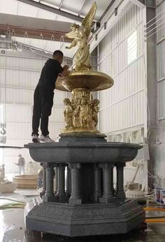 a man standing on top of a golden fountain in a warehouse area with other workers nearby