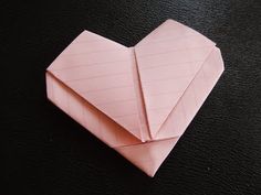 an origami heart shaped piece of paper on a black surface with one folded in half