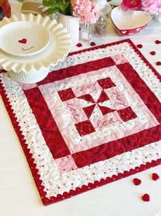 a quilted table runner with hearts on it and flowers in the vases next to it