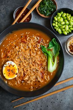 a bowl of ramen with chopsticks and bowls of vegetables on the side