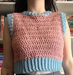 a woman standing in front of a bookshelf wearing a pink and blue knitted top