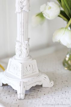 a white vase with flowers in it sitting on a table next to a candle holder