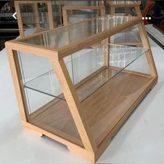 a wooden display case with glass shelves on the top and bottom, sitting on a white surface