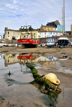 the boats are docked in the harbor by the water's edge, and one is laying on its side